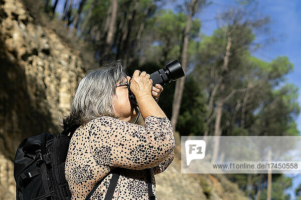 older white-haired woman taking pictures in a forest