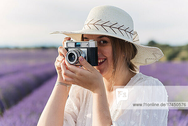 Blonde woman taking a photo with a vintage camera in a lavender field.
