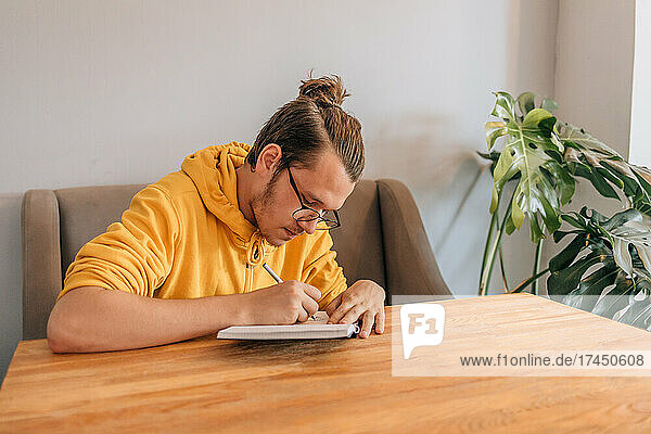 Teenager young man is writing in notebook in cafe. Lifestyle shot.