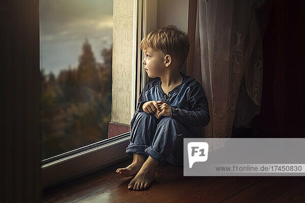 Small boy in blue clothes sitting on the floor by window and loo