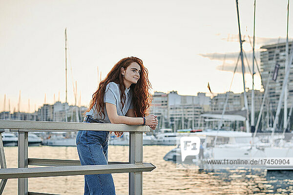 Young redhead woman looks to the sea in a seaport of a city