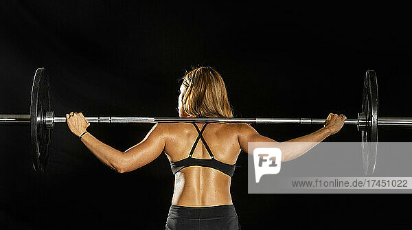 woman training with barbell on a black background in gym