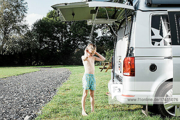 boy enjoying outdoor shower whilst camping in a campervan