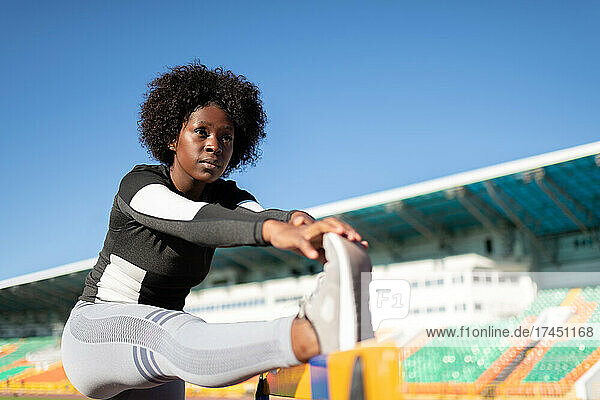 African American sportswoman stretching near barrier