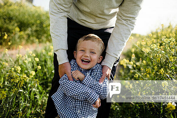 Close Up of Young Boy Laughing While Dad Holds Him in Wildflower Field