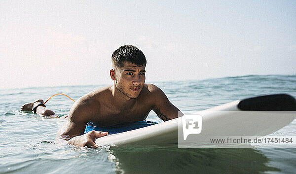 Young brunette surfer waiting for a wave on his board in the sea.