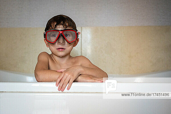 Portrait young boy leaning on bathtub edge wearing a diving mask