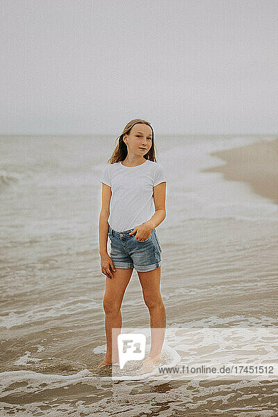A girl in a white T-shirt stands by the Baltic Sea.