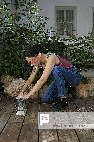 A young girl using an electric sander in the garden at home