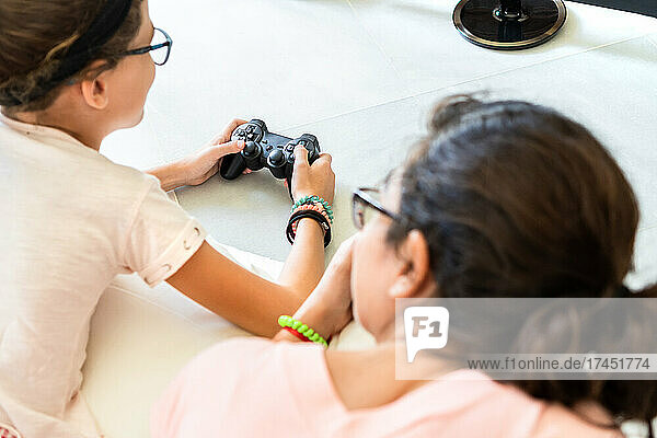 Unrecognized mother and daughter lying on floor playing video games.