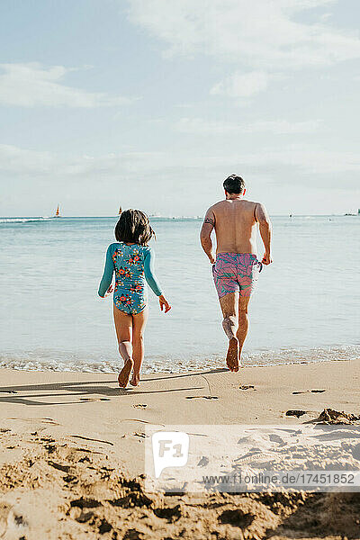 Father and daughter run and play in ocean on beach in Waikiki