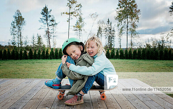 brother and sister hugging on a skateboard playing in the garden