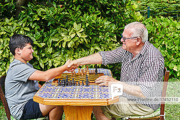 Grandfather and grandson shaking hands over chessboard