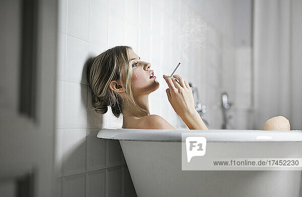young woman smokes a cigarette in the bathtub