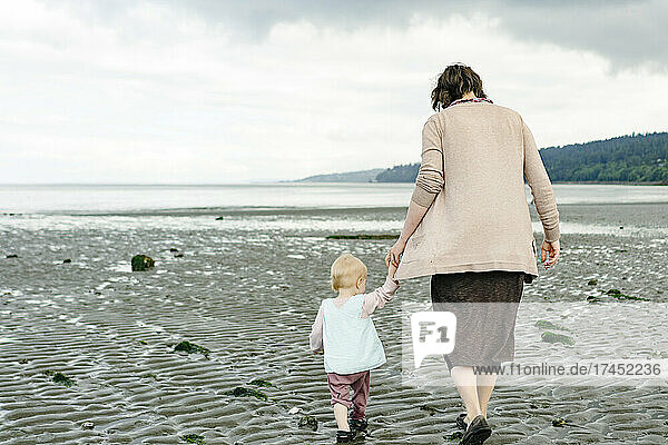 View from behind of a mother and daughter holding hands on the beach