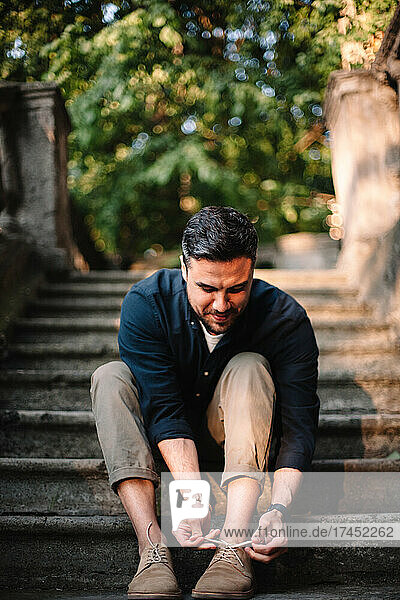 Happy man tying shoelace sitting on steps in city in summer