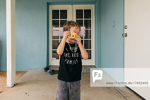 Four year old Caucasian boy plays pretend with toy camera in backyard