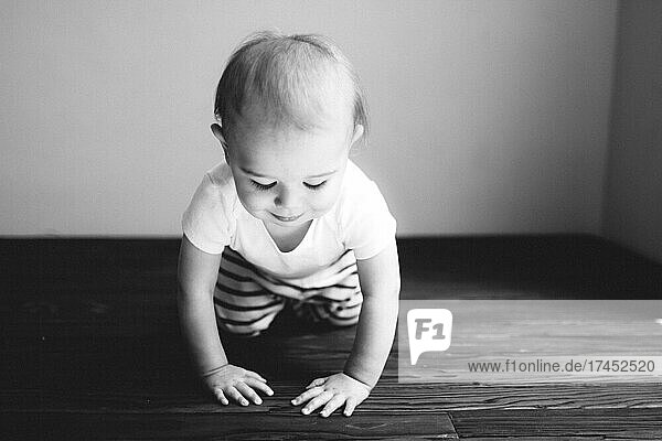 Black and white photo of a baby boy crawling on a wood floor