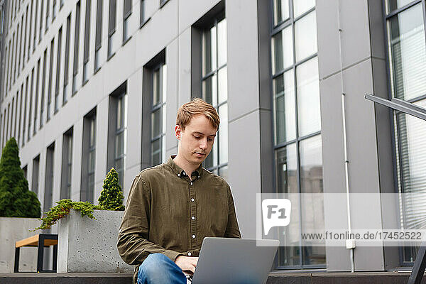 man working on laptop sitting on the stairs of business center