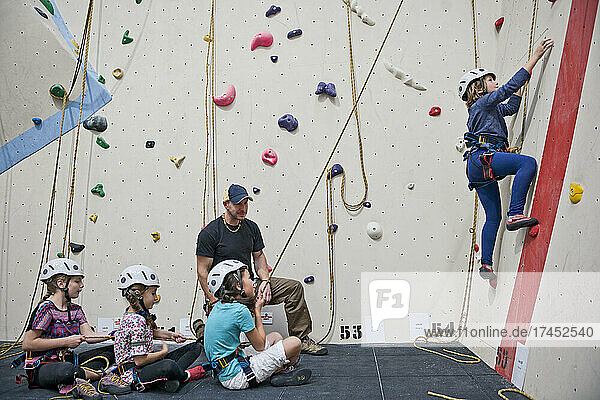 climbing coach assisting group of girls at indoor climbing wall