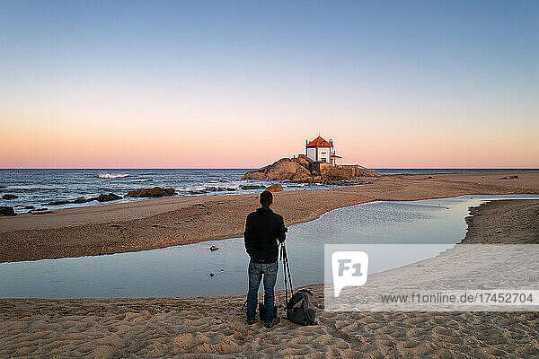Man photographing beautiful Senhor da Pedra chapel on the beach