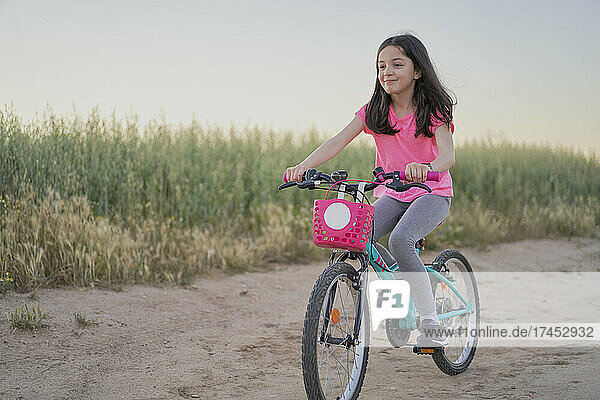 Happy girl riding a bike on a road in the field at sunset