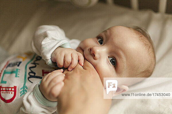 Infant baby biting hand of mother while teething