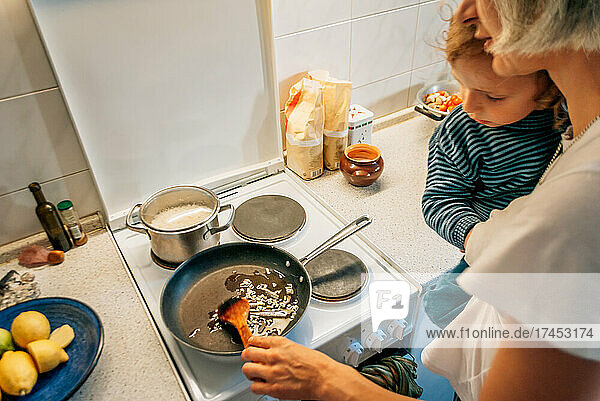 A woman cooks dinner at home with a child in her arms