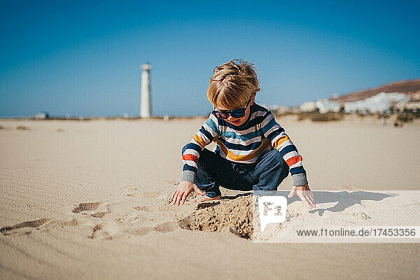 Young boy wearing sunglasses playing with sand at beach