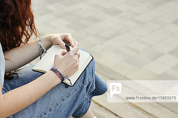 Close-up of a young redhead woman writing in a notebook outdoors