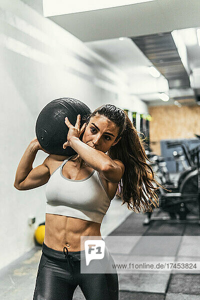 woman walking with ball shot weight on shoulder in gym doing crossfit