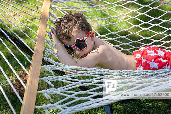 Young boy relaxing on his stomach in a hammock wearing sunglasses
