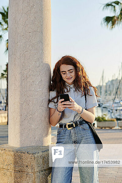Young redhead woman looks at her mobile in a seaport
