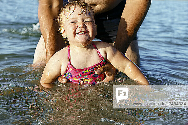 The smiling girl in pink swimsuit swims holding daddy's hands