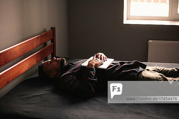 Exhausted man with laptop lying on bed at home