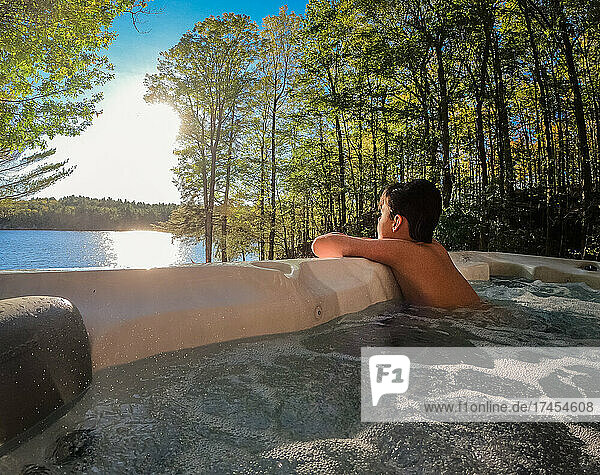 Young boy relaxing in a cottage hot tub with a lake view.