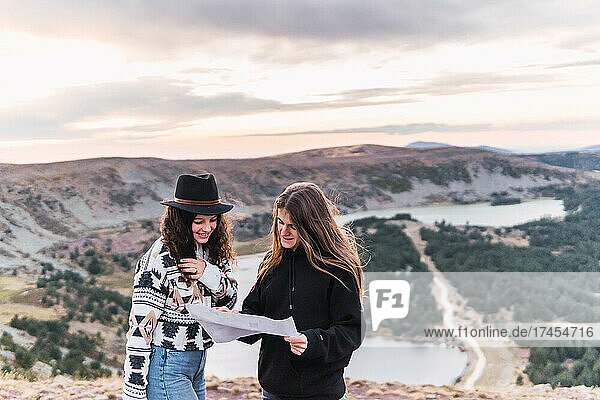 two women looking at a map standing by a lake with mountains