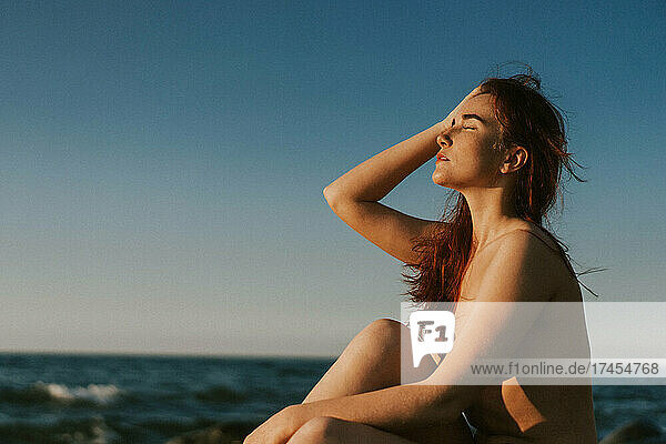 young woman sitting naked by the sea