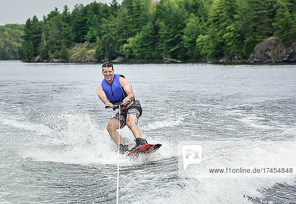 Man wake boarding while being pulled by a boat on a lake.