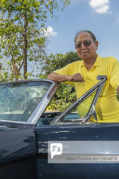 Senior adult posing proud with his restored convertible car