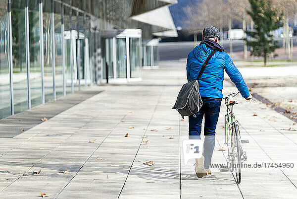 Senior man wheeling bicycle on city street holding a handbag