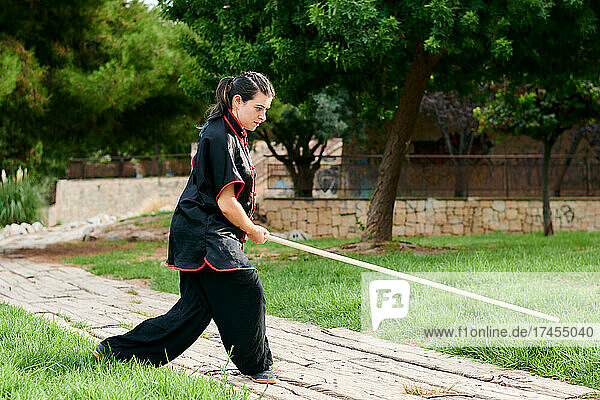 Woman training kung fu with a stick in a park