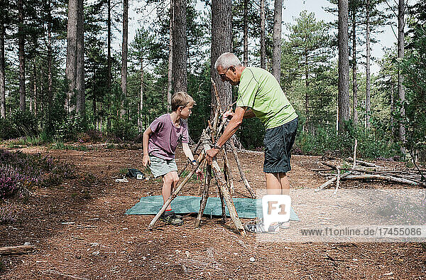 grandfather helping grandson build a camp in the forest