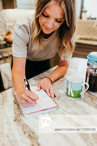 Woman writes in planner in kitchen while waiting for coffee