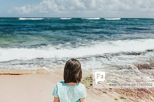 Young girl watches ocean waves from a beach in Oahu
