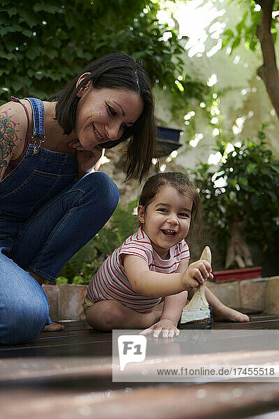 A girl and her mother have fun painting the wood on the floor.