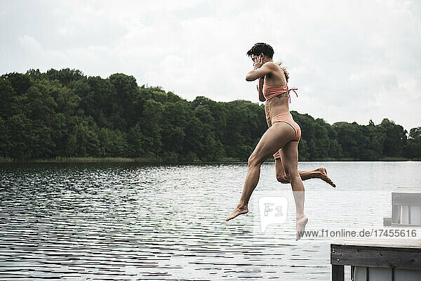 Friends jumping in lake in Poland in orange swimsuit in summer