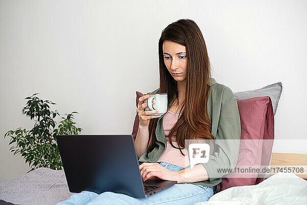 Young woman relaxing at home  using laptop and drinking coffee.