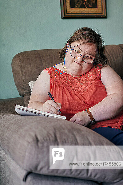 Adult woman with down syndrome writes in a notebook on a couch at home