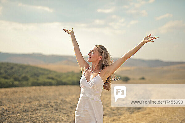 young woman breathes air with open arms in the countryside